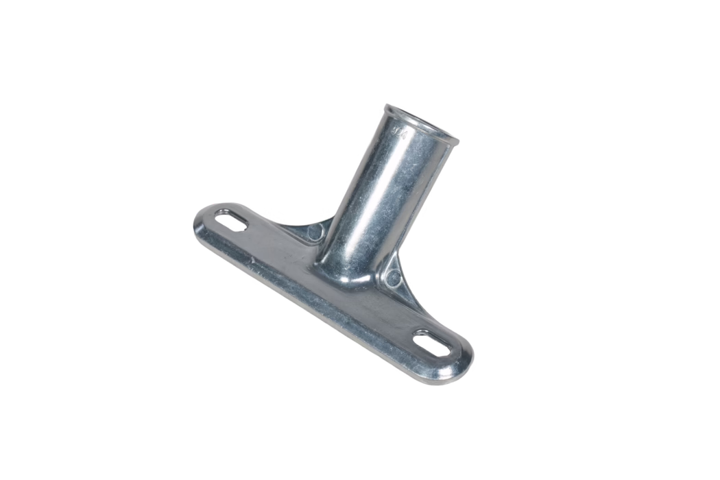 Pajarito_Dummy_Handle for squeegee with threaded insert_186422_2026-03 Close-up of a zinc-plated angled metal mounting bracket. The component features a flat rectangular base with two elongated oval mounting slots and a welded cylindrical sleeve set at an angle to the base. The surface has a bright, slightly textured galvanized finish with minor tool marks and a small stamped marking near the sleeve. Reinforcing ribs are formed where the sleeve meets the base, and rounded edges and countersunk areas are visible for fastener clearance. The bracket is photographed on a white background and is clearly intended to accept a tubular rod or pole and be secured with screws or bolts through the slotted holes.