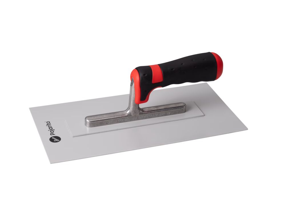Pajarito_Dummy_Plastic smoothing trowel Soft Performance Line_013138_013139_2021-02 A metal trowel with a black and red ergonomic handle, resting on a flat rectangular surface. The blade is shiny and made of stainless steel, and the handle has a textured grip for easy handling. The brand logo is visible on the surface beneath the trowel.
