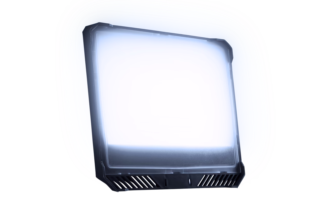 A slightly tilted rectangular LED panel light with a dark plastic frame and a frosted diffuser emitting a cool white-blue glow; the bottom edge features angled ventilation slits and mounting notches. The fixture is isolated on a white background, showing subtle reflections on the surface and a soft halo of light.