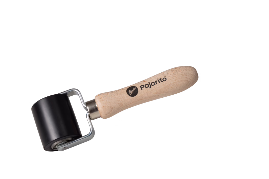 A black rubber roller with a wooden handle, labeled 'Pajarito'. The roller is mounted on a metal frame and has a smooth, glossy surface. It is angled slightly to the right, showcasing its design.