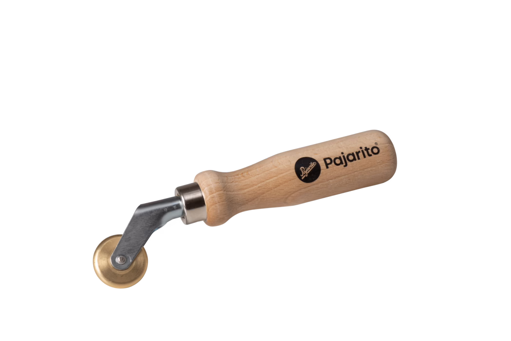 Hand tool with a smooth, rounded beech wood handle printed with the brand name 'Pajarito', a short metal shank and a small brass roller wheel mounted on a swiveling bracket; designed to press and smooth seams, wallpaper edges, leather or adhesive surfaces. The natural wood grain and black logo are clearly visible. Photograph on a plain white background.