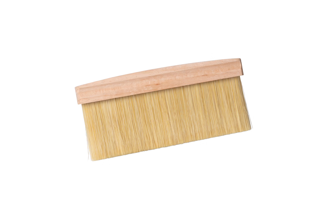 A wide flat brush with a light wooden handle and dense beige synthetic bristles, shown on a white background at a slight diagonal. The brush is typically used for wallpapering, dusting or applying varnish; the long closely packed bristles are fixed to a simple unvarnished wooden base.